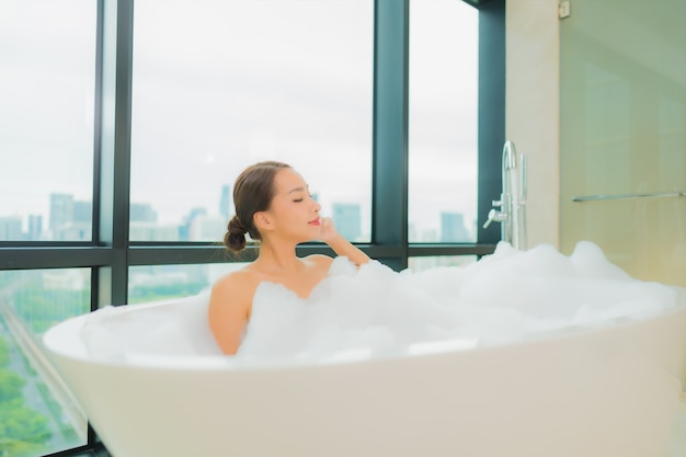 Женщина портрета красивая молодая азиатская ослабляет отдых улыбки в ванне в интерьере ванной комнаты