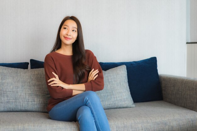 肖像画の美しい若いアジア女性はリビングルームのインテリアのソファーで笑顔をリラックスします。