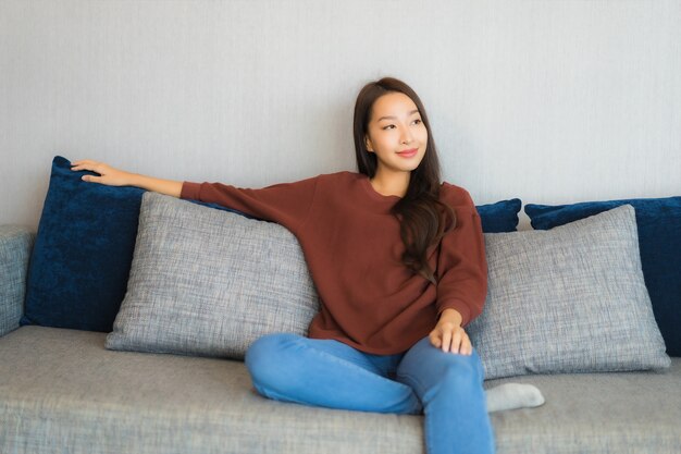 세로 아름 다운 젊은 아시아 여자는 거실 인테리어에 소파에 미소를 긴장