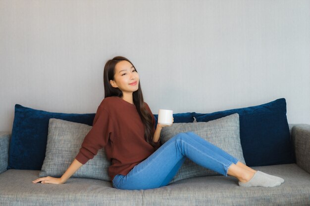 세로 아름 다운 젊은 아시아 여자는 거실 인테리어에 소파에 미소를 긴장