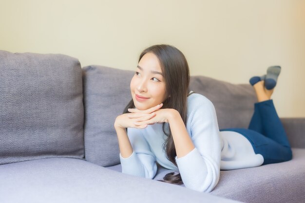 Женщина портрета красивая молодая азиатская ослабляет улыбку на софе в живущей комнате