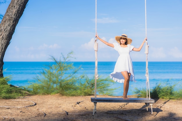 肖像画美しい若いアジアの女性は休暇中の自然旅行のためにビーチの海の海の周りのスイングで笑顔をリラックス