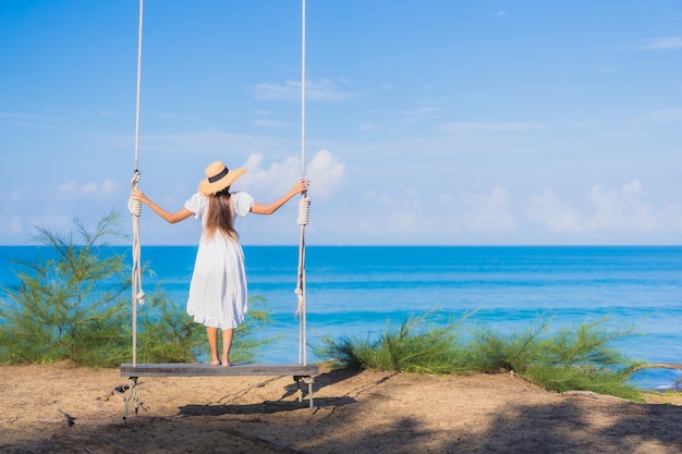 肖像画美しい若いアジアの女性は休暇中の自然旅行のためにビーチの海の海の周りのスイングで笑顔をリラックス