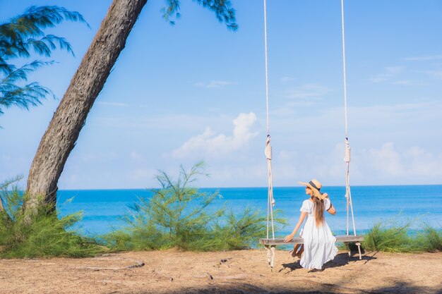 肖像画美しい若いアジアの女性は休暇中の自然旅行のためにビーチの海の海の周りのスイングで笑顔をリラックス