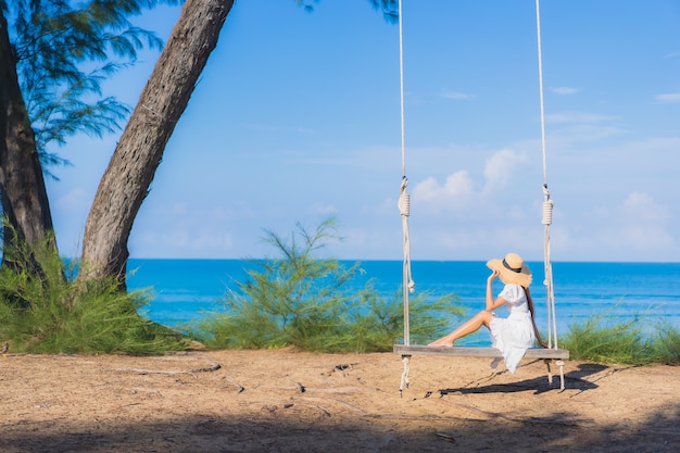 肖像画美しい若いアジアの女性は休暇中の自然旅行のためにビーチの海の海の周りのスイングで笑顔をリラックス