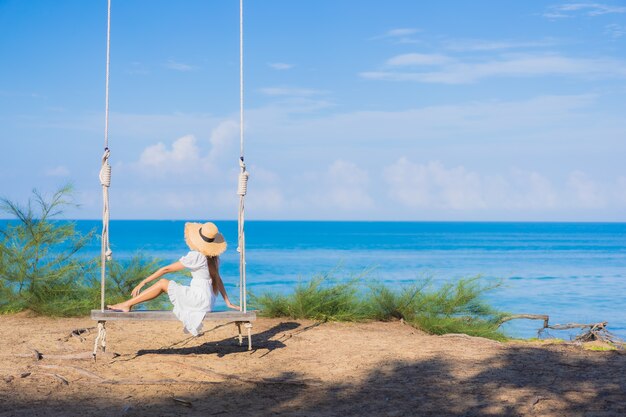 肖像画美しい若いアジアの女性は休暇中の自然旅行のためにビーチの海の海の周りのスイングで笑顔をリラックス