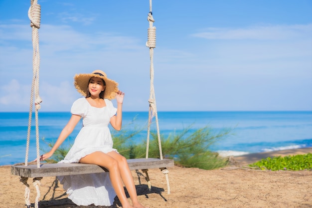 肖像画美しい若いアジアの女性は休暇中の自然旅行のためにビーチの海の海の周りのスイングで笑顔をリラックス