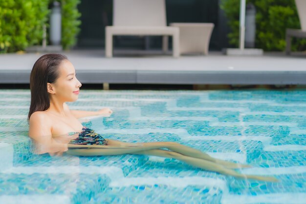 Портрет красивой молодой азиатской женщины расслабляется на бассейне в курорте гостиницы