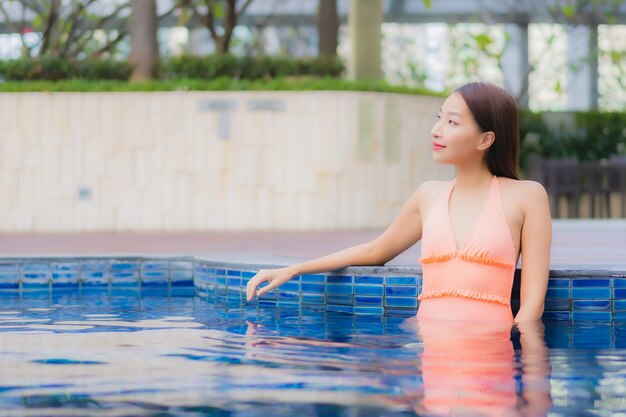 Портрет красивой молодой азиатской женщины расслабляется на бассейне в курорте гостиницы