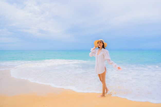 Портрет красивой молодой азиатской женщины ослабляя вокруг океана моря пляжа в каникулах перемещения