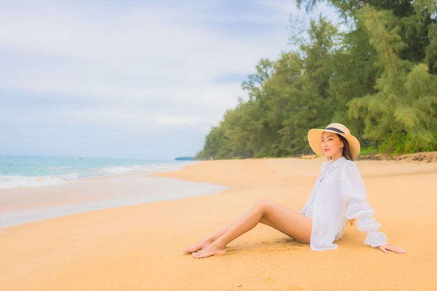 Портрет красивой молодой азиатской женщины ослабляя вокруг океана моря пляжа в каникулах перемещения