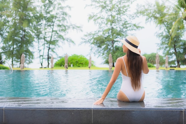 바다에 가까운 호텔 리조트에서 야외 수영장 주변에서 편안한 아름 다운 젊은 아시아 여자의 초상화