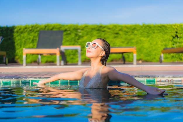 Портрет красивой молодой азиатской женщины ослабляя вокруг открытого бассейна в курорте гостиницы