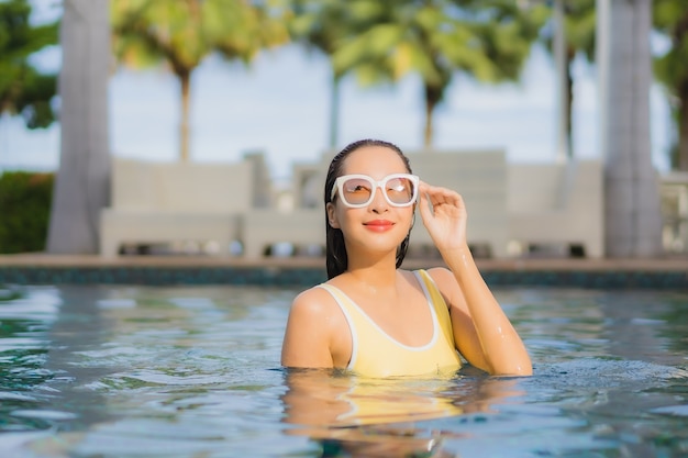 Bella giovane donna asiatica del ritratto che si rilassa all'aperto nella piscina in viaggio di festa