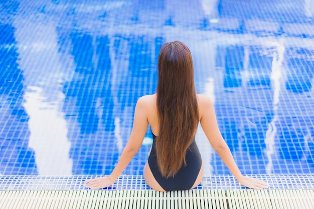 Портрет красивой молодой азиатской женщины расслабляя вокруг открытого бассейна в курорте гостиницы