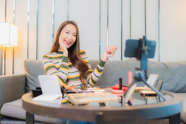 Portrait of beautiful young asian woman reviews and uses cosmetics on sofa