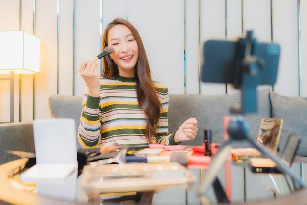 Portrait of beautiful young asian woman reviews and uses cosmetics on sofa