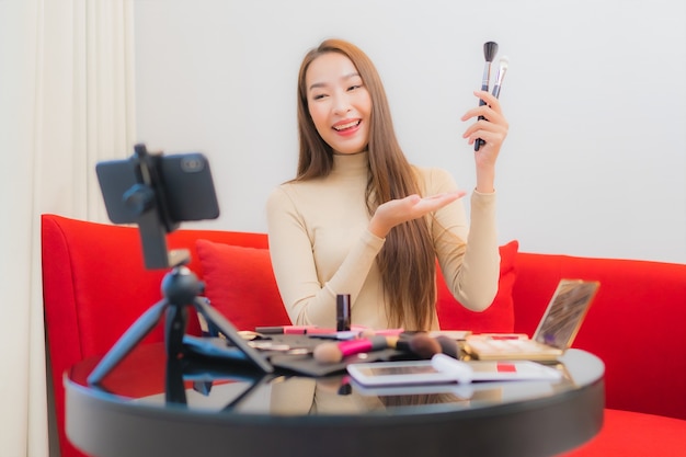 Portrait of beautiful young asian woman reviews and uses cosmetics on sofa