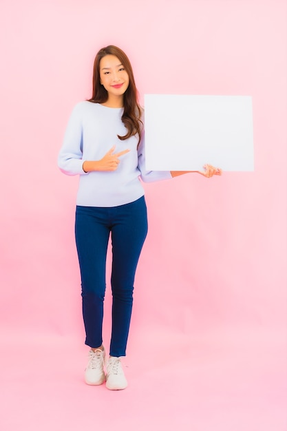 Portrait beautiful young asian woman show empty white billboard for text on pink color wall