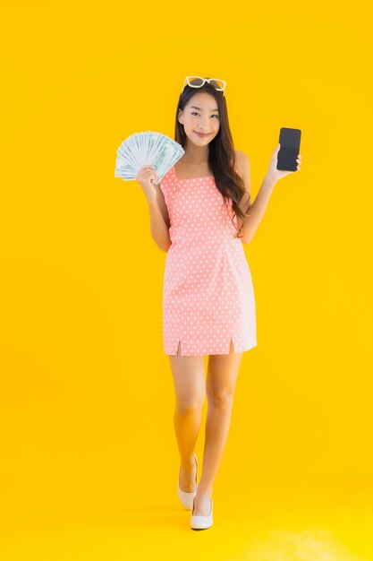 肖像画の美しい若いアジアの女性はモバイルスマートフォンでたくさんの現金とお金を表示します。