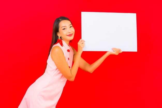肖像画美しい若いアジアの女性は赤い壁に白い空の看板を表示します