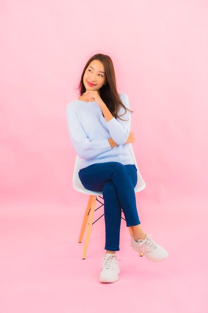 Женщина портрета красивая молодая азиатская сидит на стуле с розовой стеной цвета