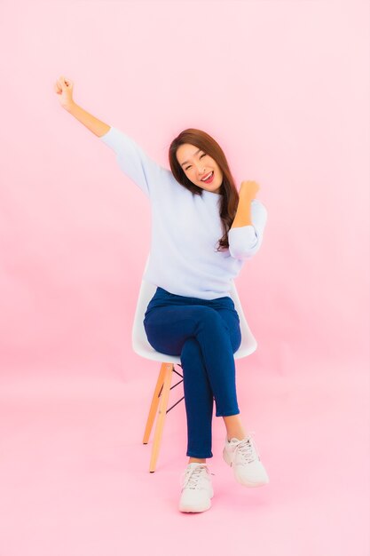 Portrait beautiful young asian woman sit on chair with pink color wall