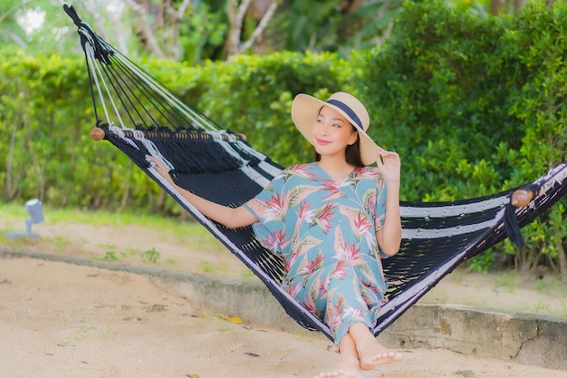 Женщина портрета красивая молодая азиатская сидит на качании гамака вокруг океана моря пляжа в отпуске
