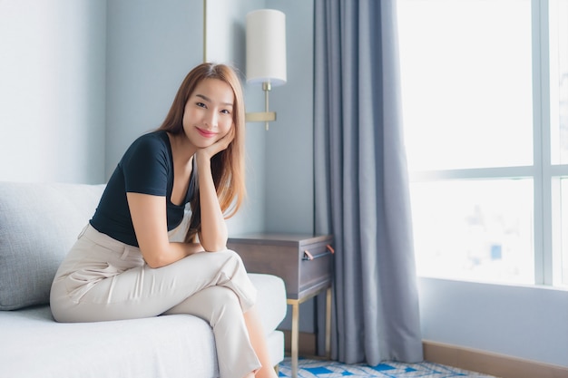 Женщина портрета красивая молодая азиатская сидит на софе ослабляет в зоне живущей комнаты