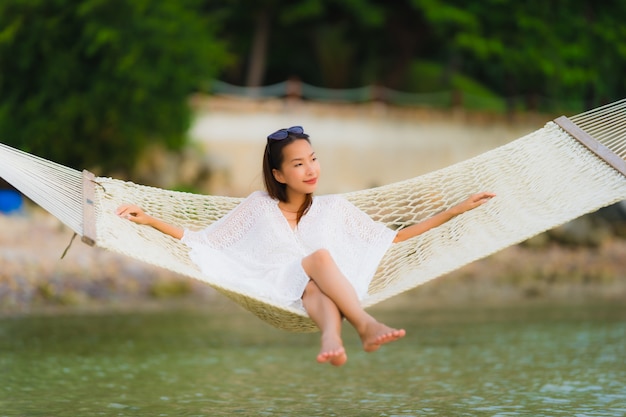 Free photo portrait beautiful young asian woman sitting on hammock around sea beach ocean for relax