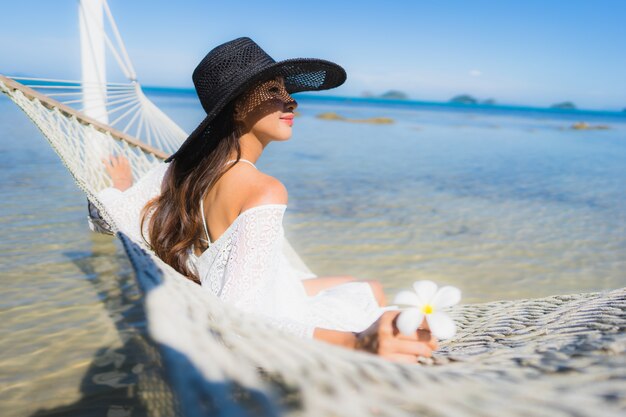 海のビーチの周りのハンモックの上に座っての肖像画美しい若いアジア女性リラックス