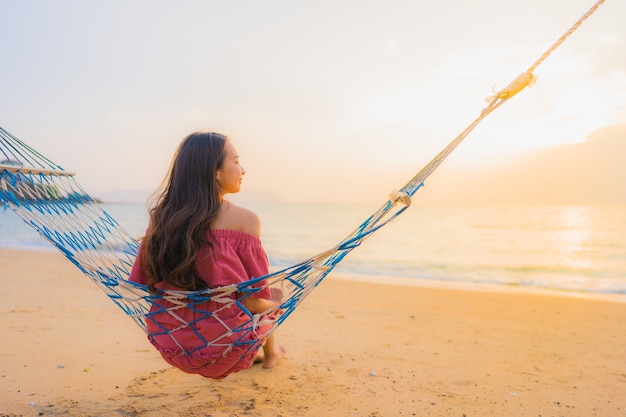 Portrait beautiful young asian woman sitting on the hammock with smile happy neary beach sea and oce