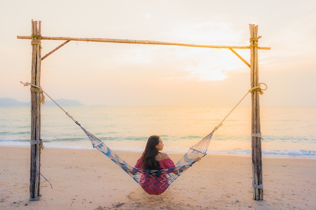 Portrait beautiful young asian woman sitting on the hammock with smile happy neary beach sea and oce