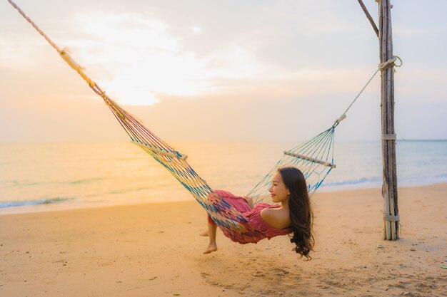 Женщина портрета красивая молодая азиатская сидя на гамаке с морем и oce пляжа neary улыбки счастливым