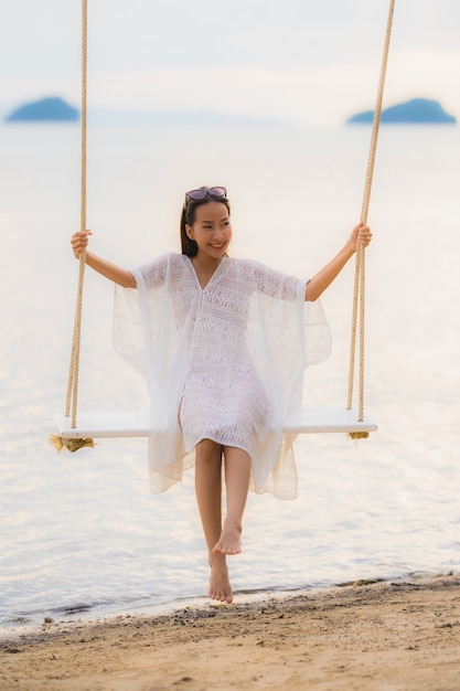 Женщина портрета красивая молодая азиатская сидя на качании вокруг океана моря пляжа для ослабляет