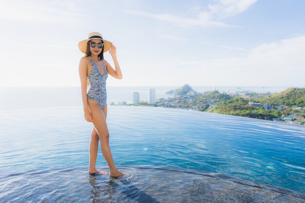 Улыбка женщины портрета красивая молодая азиатская счастливая ослабляет вокруг бассейна в курорте гостиницы для отдыха