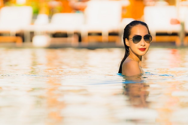 Foto gratuita il bello giovane sorriso asiatico della donna del ritratto felice si rilassa intorno alla piscina nella località di soggiorno dell'hotel per svago