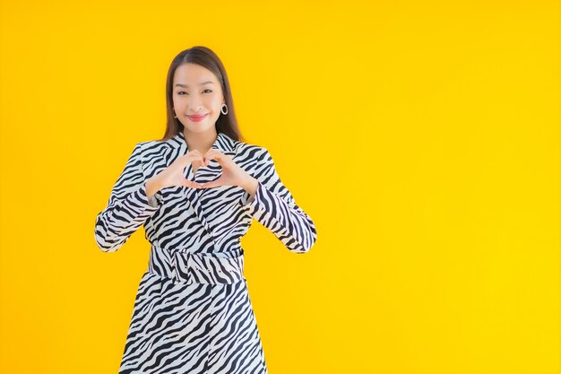 肖像画の美しい若いアジア女性は黄色のアクションに満足して笑顔します。