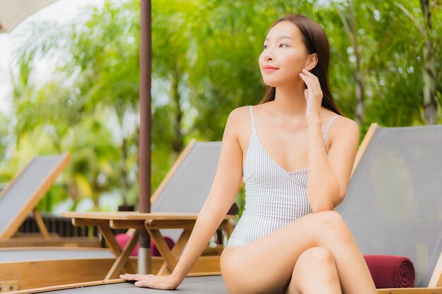 Улыбка женщины портрета красивая молодая азиатская ослабляет вокруг открытого бассейна в курортном отеле на отключении перемещения каникул праздника