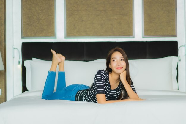 Улыбка женщины портрета красивая молодая азиатская ослабляет на кровати в интерьере спальни