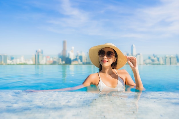 Улыбка женщины портрета красивая молодая азиатская ослабляет отдых вокруг открытого бассейна с видом на город