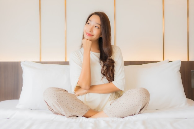 세로 아름 다운 젊은 아시아 여자 미소 침실 인테리어에 침대에서 레저 휴식