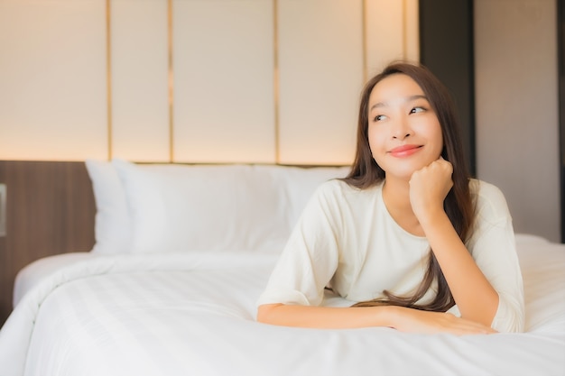 Улыбка женщины портрета красивая молодая азиатская ослабляет отдых на кровати в интерьере спальни