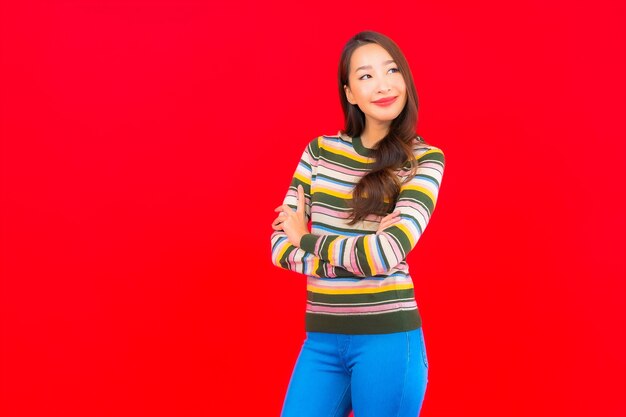 Улыбка женщины портрета красивая молодая азиатская с действием на красной изолированной стене