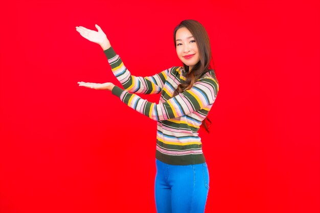 Улыбка женщины портрета красивая молодая азиатская с действием на красной изолированной стене