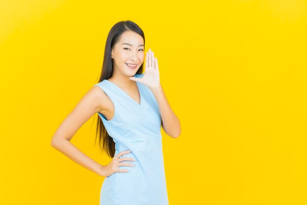 Улыбка женщины портрета красивая молодая азиатская с действием на стене желтого цвета