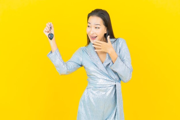 Portrait beautiful young asian woman smile with car key on yellow wall