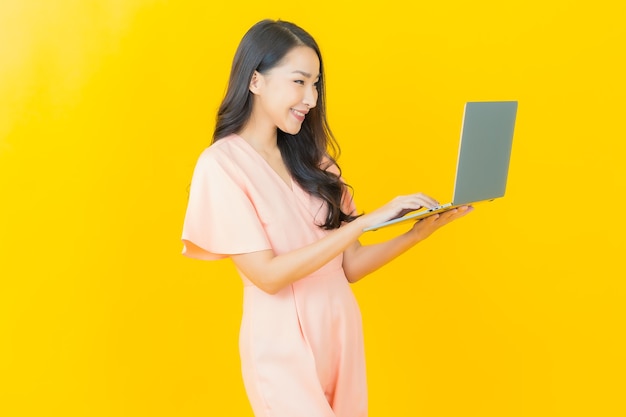 Улыбка женщины портрета красивая молодая азиатская с компьтер-книжкой компьютера на изолированной стене