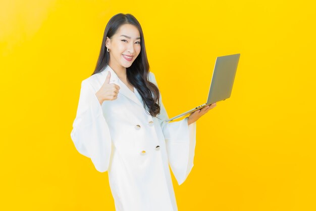 노란 벽에 컴퓨터 노트북을 들고 웃는 아름다운 젊은 아시아 여성의 초상화