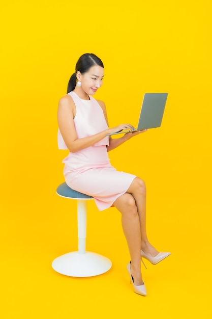 Portrait beautiful young asian woman smile with computer laptop on yellow